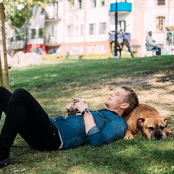 man som ligger ner i gräset och vilar huvudet på en hund